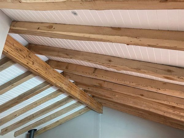 Exposed timber roof beams over a white panelled ceiling