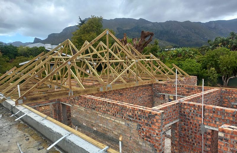 Timber roof trusses erected on a new brick build with mountains behind
