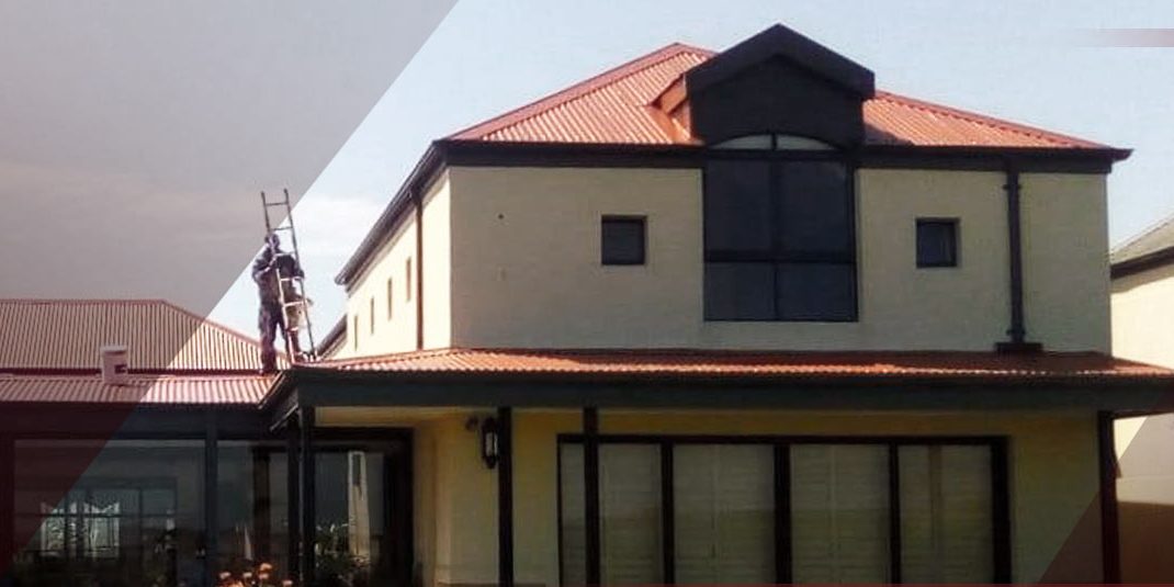 Rome Roofing worker on a ladder inspecting the tiled roof of a double-storey home
