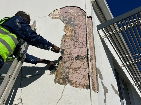 Painter working from a ladder on exterior wall preparation
